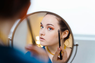 Young beautiful female makeup artist sitting at table with eyeshadow palette applying makeup with brush