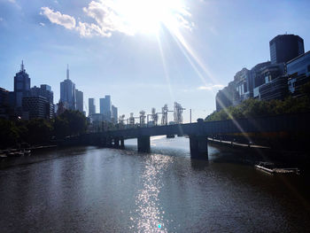 Bridge over river by buildings against sky in city