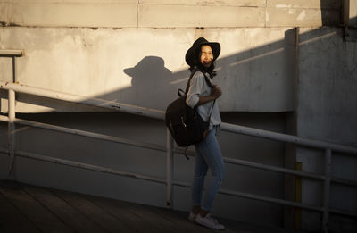 Portrait of young woman standing on staircase against wall