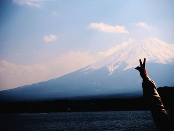 Cropped hand showing peace sign by lake against mount fuji