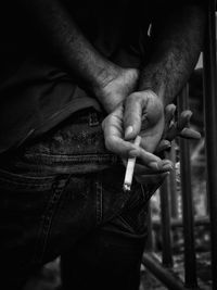 Midsection of man holding cigarette while standing outdoors