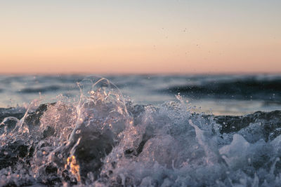 Sea waves splashing on rocks against sky during sunset