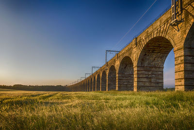 Arch bridge on field against sky during sunset