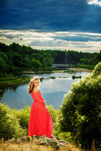 Portrait of woman standing by lake against trees