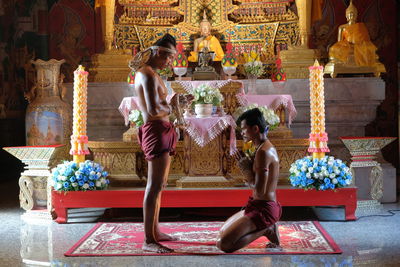 Side view of shirtless men praying in buddhist temple