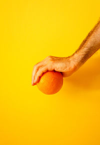 Orange in hand on yellow wall ii