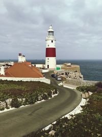 Lighthouse amidst sea and buildings against sky