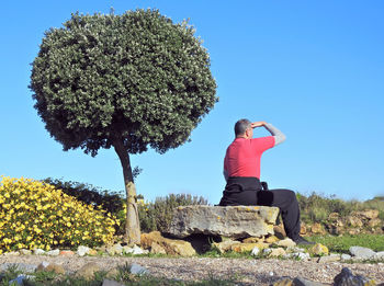 Man sitting on rock against sky