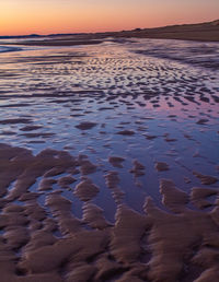 Surface level of beach against sky during sunset