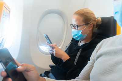 A young woman wearing face mask, using smart phone while traveling on airplane. new normal travel