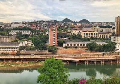 Arch bridge over river by buildings in city against sky