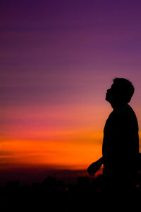 Silhouette man sitting against orange sky