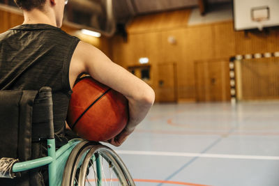 Girl sitting on wheelchair holding basketball at sports court