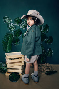 Boy child traveler in a hat stand on wooden boxes in a studio on a green background