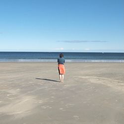 Rear view of woman standing at beach against clear sky