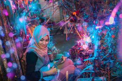 Young woman sitting in illuminated traditional clothing holding umbrella at night