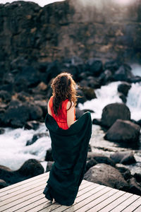 Rear view of woman looking away while sitting on wood