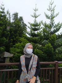 Portrait of man standing by railing against trees