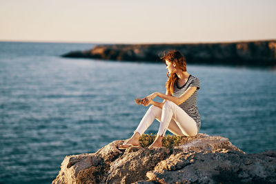 Woman sitting on rock by sea against sky