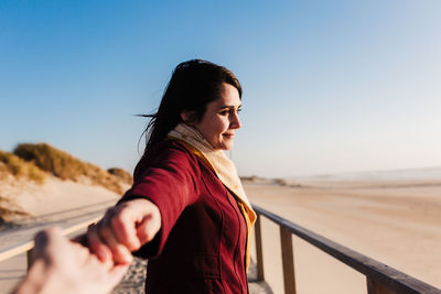 Smiling young woman holding hands against sky