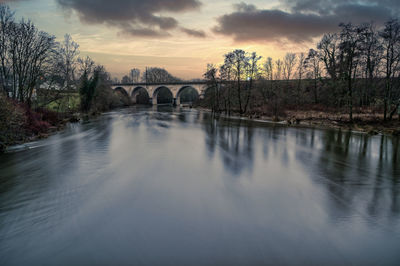 Arch bridge over river against sky during sunset