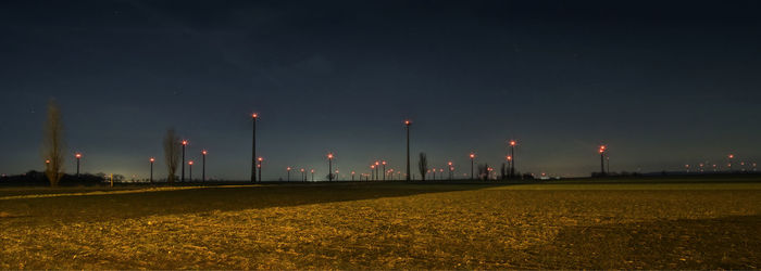 Illuminated street lights on field against sky at night