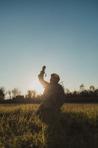 Rear view of man with arms outstretched on field against clear sky