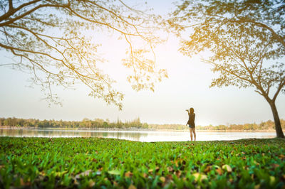 Man standing on grass by lake against sky