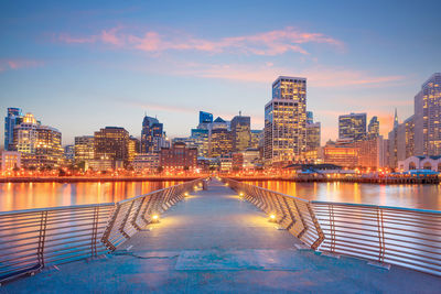 Illuminated buildings by swimming pool against sky at dusk