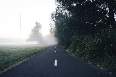 Wet road by trees against sky