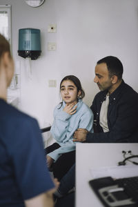 Father with daughter discussing with female nurse during visit in clinic