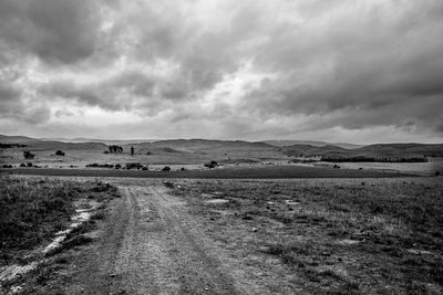 Dirt road on field against sky