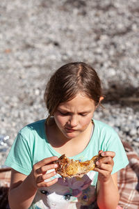 Young girl with a chicken leg in her hand at a picnic .