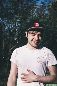 Young man wearing hat standing against trees