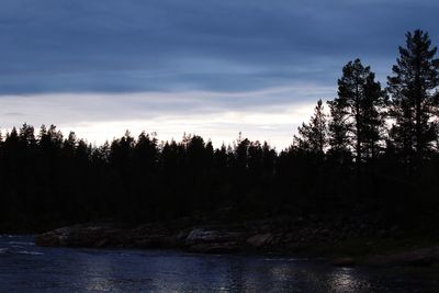 Silhouette trees by lake in forest against sky at sunset