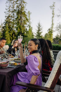 Side view of smiling woman holding drink glass while sitting with friends during dinner party