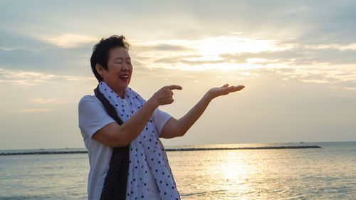 Senior woman gesturing at beach during sunset