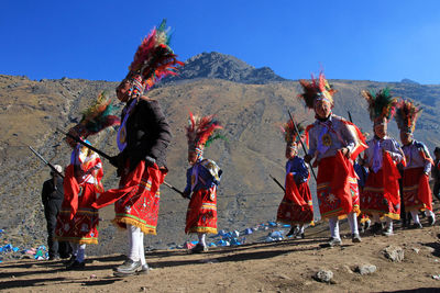 People in traditional clothing dancing on sand against mountains and sky