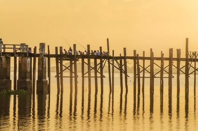 People fishing while sitting on wooden bridge