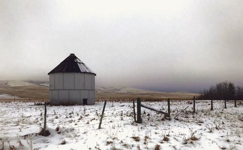 Barn on snowy field against sky during winter