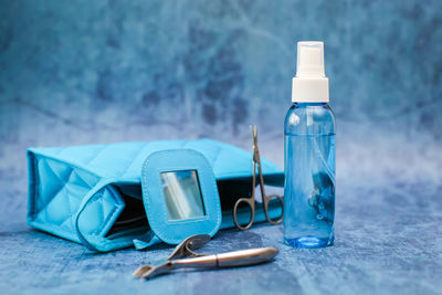 Close-up of small spray bottle with clutch bag and tweezers on blue table