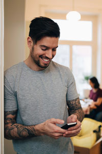 Smiling man using mobile phone while leaning on doorway at new home