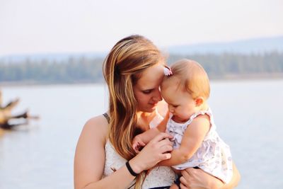 Close-up of mother holding baby girl against sea