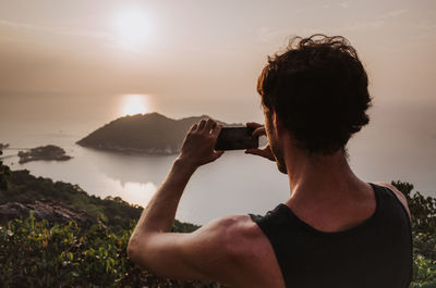 Rear view of man photographing against sky during sunset