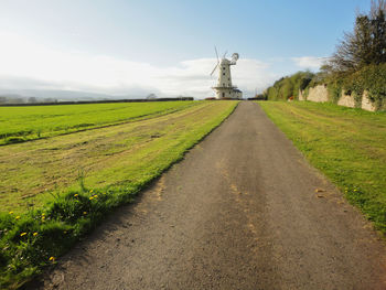 Empty road leading towards traditional windmill on field against sky