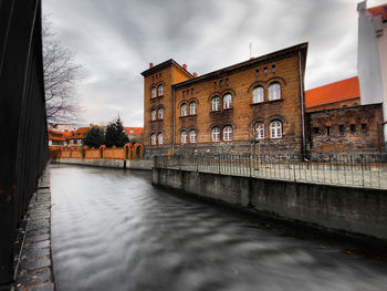 Canal by buildings in city against sky