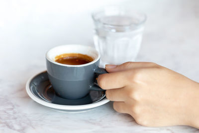 Espresso cup in female hand and glass of water on the marble table. morning ritual at the cafe.