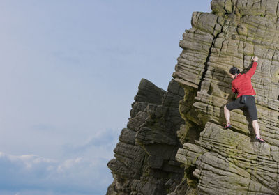 Low angle view of woman standing on rock against sky