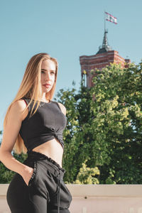 Thoughtful young woman standing on balcony against clear blue sky