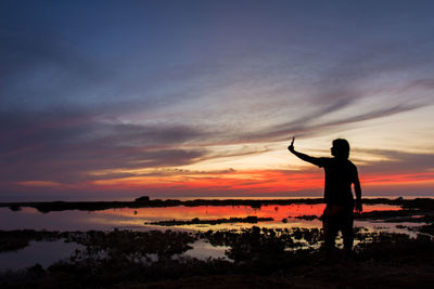 Silhouette man taking selfie on land against sky during sunset